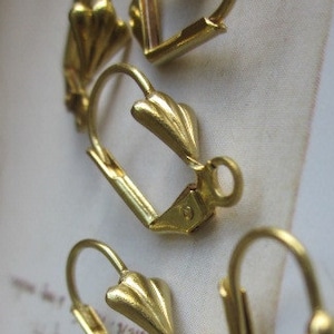 May include: Close-up of several gold-colored leverback earring findings. The findings have a decorative, fan-shaped design at the top of the lever. The earring findings are made of metal and are designed for jewelry making.
