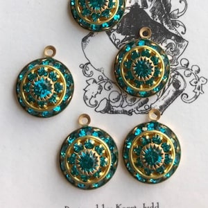 May include: Five teal and gold-colored round charms with a floral design are displayed on a white tag with a ribbon. The tag features a black and white illustration of a woman in a dress. The charms have a small loop at the top.