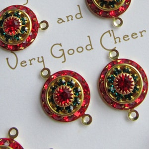 May include: A set of red and green Christmas-themed jewellery charms with gold accents. The charms feature a round design with red and green rhinestones. The charms are arranged on a white card with the text "Wishing You Health, Happiness and Very Good Cheer".