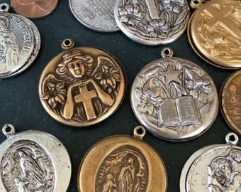 Peut inclure: Une collection de médaillons religieux vintage avec différents motifs, dont une croix, un ange et un livre. Les médaillons sont en métal argenté et doré et présentent des détails complexes.