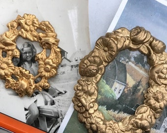 Könnte beinhalten: Zwei goldfarbene Metallkränze mit floralen Designs. Die Kränze liegen auf zwei alten Postkarten. Eine Postkarte zeigt ein Paar auf einem Schwarzweißfoto. Die andere Postkarte zeigt ein Aquarellbild eines Bauernhauses.