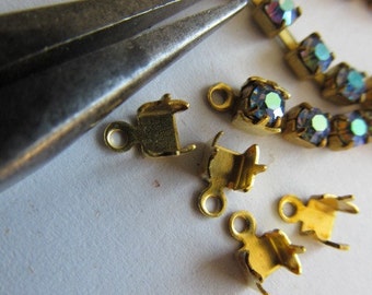 May include: Close-up of gold-toned metal clasps for jewelry making. The clasps are small and have a simple design. A pair of pliers is also visible in the image.