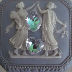 May include: A blue and white ceramic trinket box with a raised design of two women dancing. The box has a heart-shaped iridescent crystal on the front.