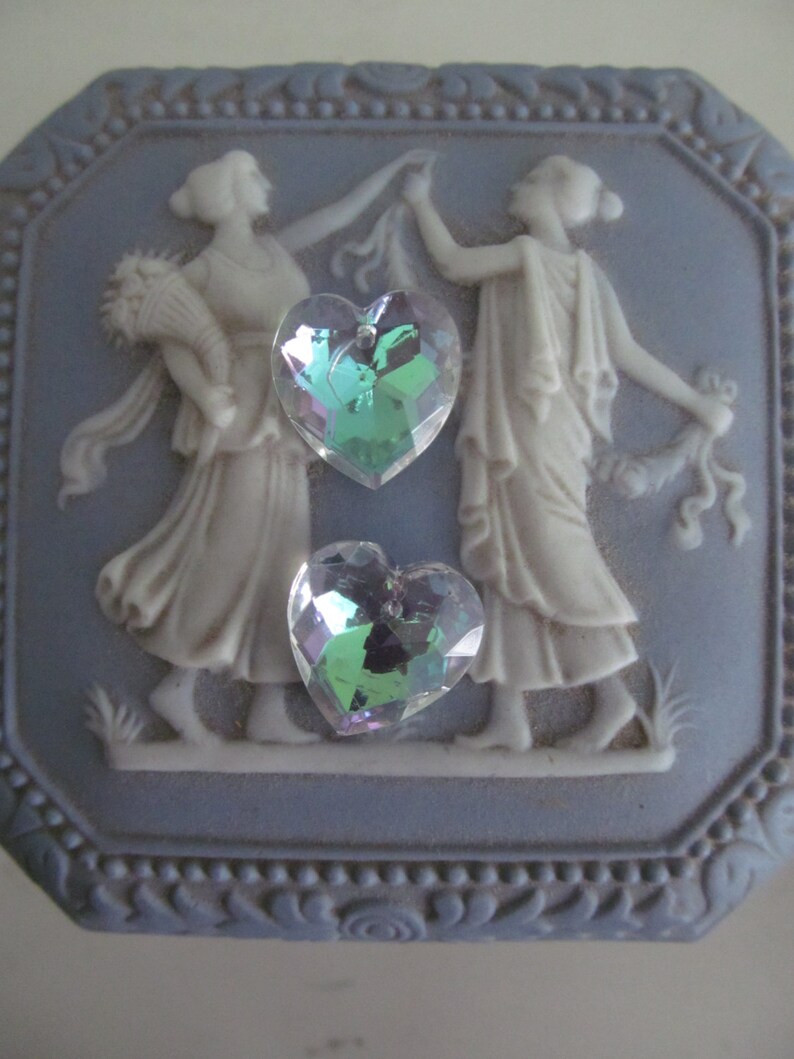 May include: A blue and white ceramic trinket box with a raised design of two women dancing. The box has a heart-shaped iridescent crystal on the front.