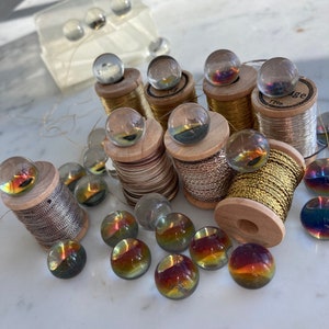 Peut inclure: Une collection de billes en verre iris&eacute;es et de bobines de fil d'or et d'argent. Les billes sont dispos&eacute;es sur une surface en marbre blanc. Les bobines de fil sont sur des bobines en bois avec des &eacute;tiquettes.