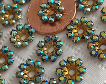May include: Close-up of several small, gold-toned flower-shaped embellishments with iridescent blue and green crystal accents. A penny is included for size comparison. These decorative elements could be used for jewelry or craft projects.