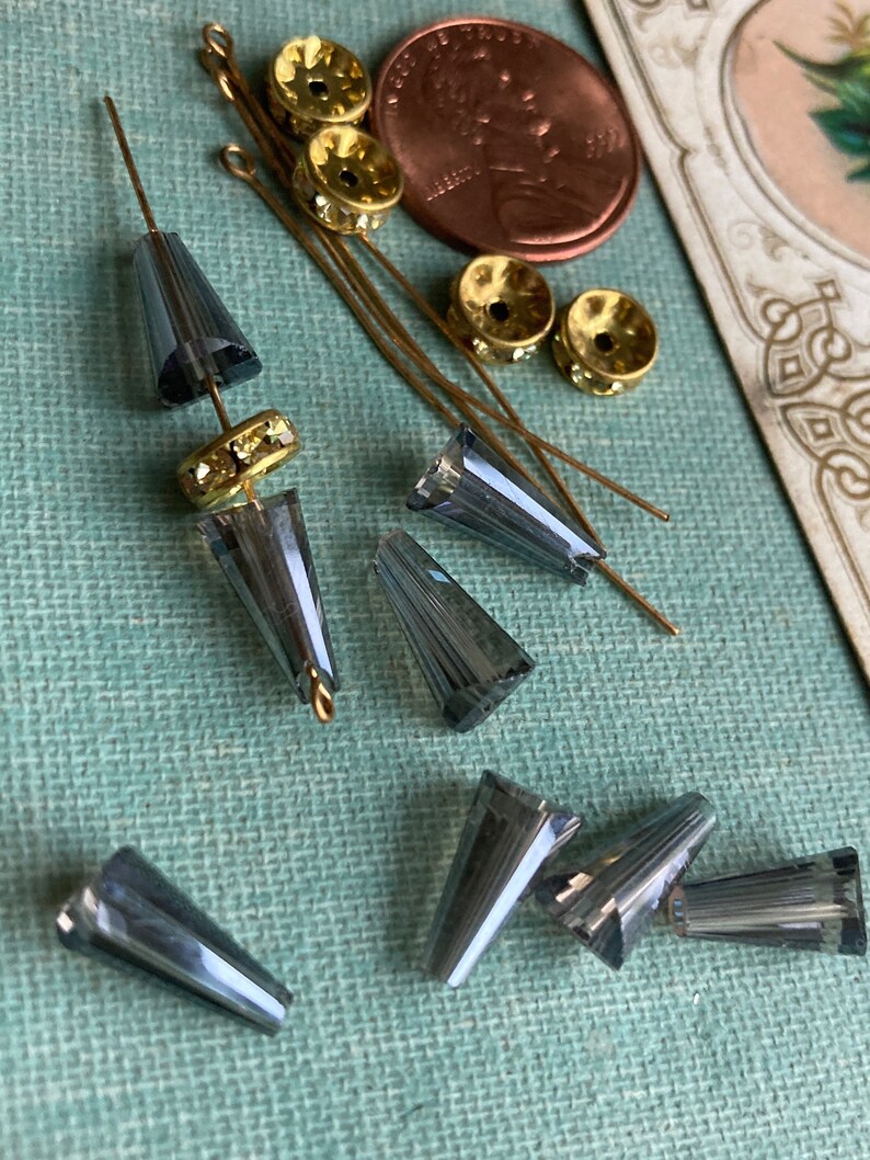 May include: A collection of grey glass cone-shaped beads with gold-toned metal bead caps and head pins.