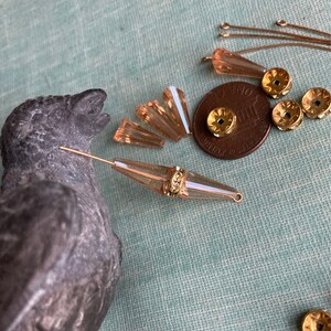 May include: Assortment of gold and peach coloured glass beads, including teardrop, round, and faceted shapes. There are also gold jump rings and a UK penny coin.