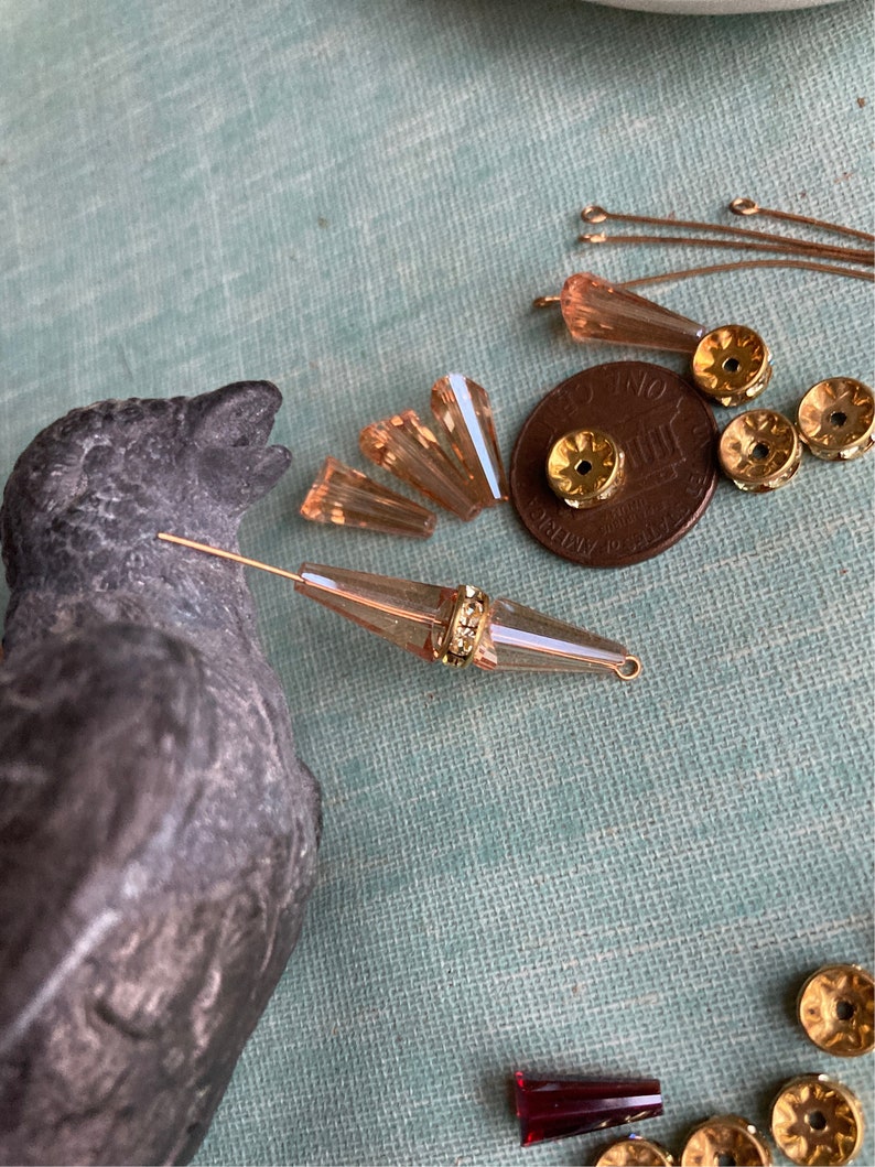 May include: Assortment of gold and peach coloured glass beads, including teardrop, round, and faceted shapes. There are also gold jump rings and a UK penny coin.