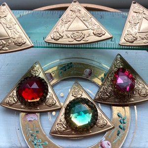 May include: Six gold-tone triangular pendants with a raised rose design. Three pendants have clear faceted gems in red, green, and pink.