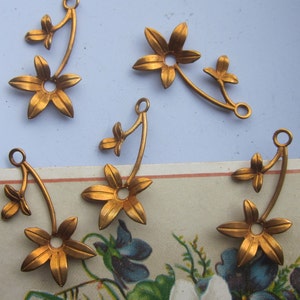 May include: Five gold-toned metal flower charms with a five-pointed star shape and a small loop at the top. The charms are attached to a stem with leaves.
