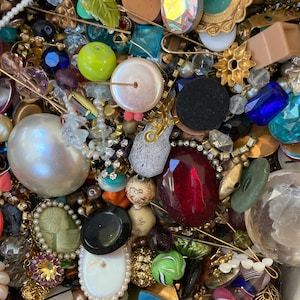 May include: A large collection of vintage buttons, beads, and other jewelry findings. The assortment includes a variety of colors, shapes, and materials, including glass, metal, plastic, and wood. There are also some small charms and decorative pieces.
