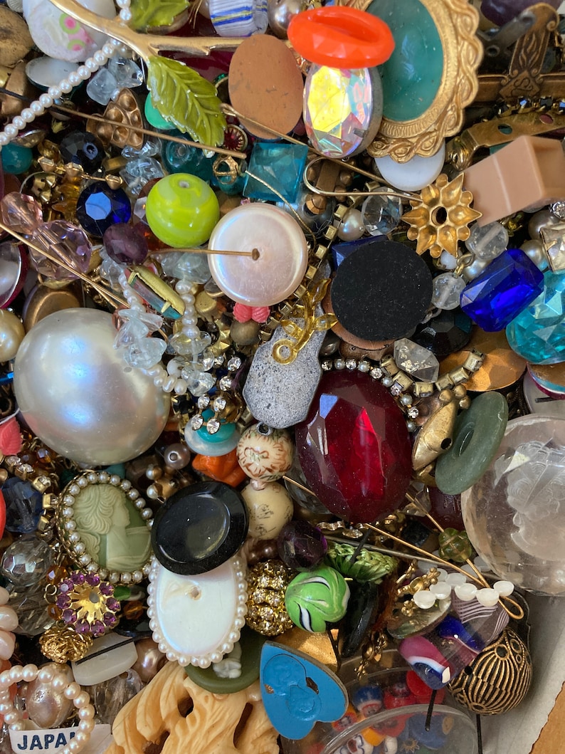 May include: A large collection of vintage buttons, beads, and other jewelry findings. The assortment includes a variety of colors, shapes, and materials, including glass, metal, plastic, and wood. There are also some small charms and decorative pieces.