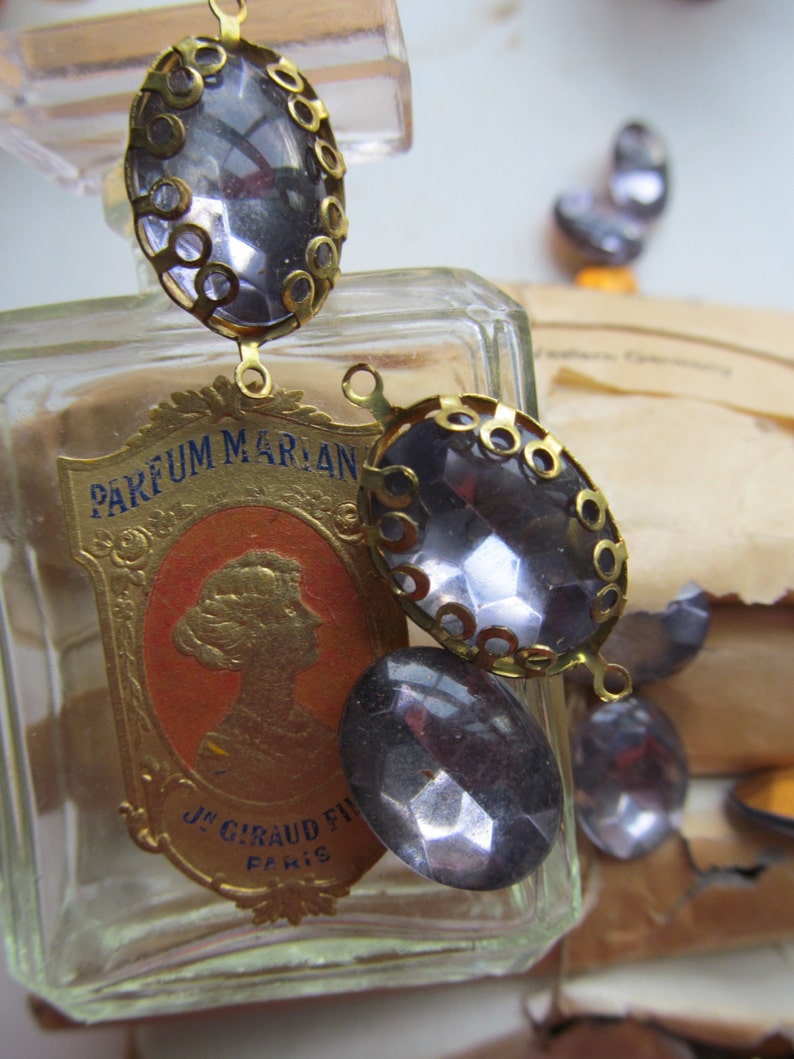 May include: A clear glass bottle with a gold label that reads "PARFUM MARIAN J. GIRAUD FILS PARIS". The bottle is decorated with a gold chain and several clear glass stones.