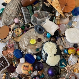 May include: A collection of colorful and eclectic jewelry making supplies, including beads, buttons, charms, and findings. The supplies are arranged in a random pattern on a white surface.