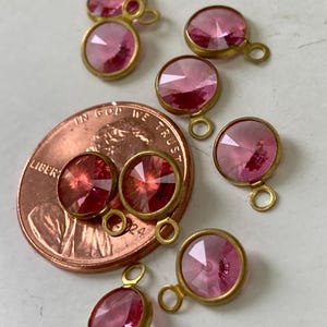 May include: A collection of pink gemstone pendants with gold-colored metal settings. The faceted stones vary in size and shape, with a small loop at the top for attaching to jewelry. A penny is included for size reference.