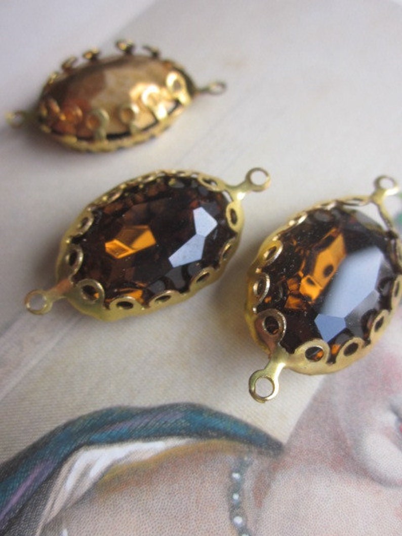 Pode incluir: Tr&ecirc;s enfeites de metal dourado com pedras de vidro &acirc;mbar de forma oval. Cada enfeite tem um design de filigrana decorativo e dois la&ccedil;os para prender a um projeto.