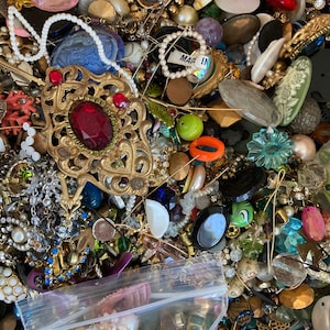 May include: A large collection of colorful and assorted buttons, beads, and jewelry findings. The items are arranged in a box and include a variety of materials, shapes, and sizes. There is a small plastic bag in the lower right corner of the image.