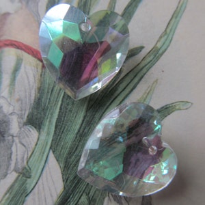 May include: Two iridescent heart-shaped crystal charms with a hole at the top for hanging. The charms are a light blue-green color with a rainbow sheen.