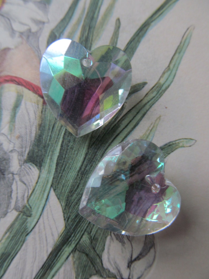 May include: Two iridescent heart-shaped crystal charms with a hole at the top for hanging. The charms are a light blue-green color with a rainbow sheen.
