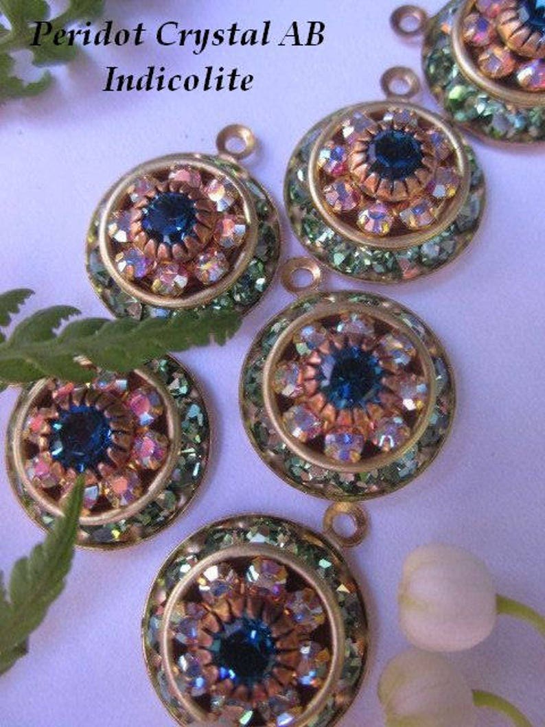 May include: Five gold-toned pendants with a round, multi-faceted, iridescent crystal center surrounded by smaller crystals. The crystals are in shades of blue, pink, and green. The text "Peridot Crystal AB Indicolite" is visible at the top of the image.