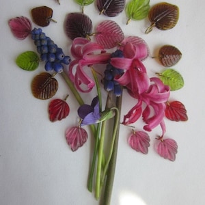 May include: A bouquet of pink hyacinths, blue grape hyacinths, and purple violets with green and brown glass leaves.