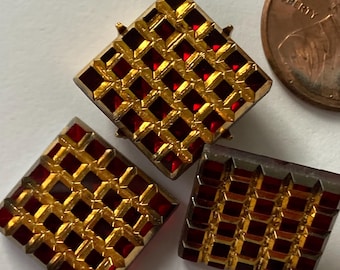 May include: Three gold-toned, diamond-shaped pendants with a grid pattern of red gemstones. One pendant has a small loop at the top. A penny is next to the pendants for size comparison. The pendants are on a white surface.