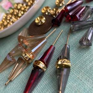 May include: Assortment of clear, red, and grey glass beads with gold accents. The beads are strung on gold wires and are ready to be used for jewellery making or other craft projects.