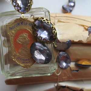 May include: A vintage glass bottle with a gold label that reads "PARFUM MARIAN J.S. GIRAUD FILS PARIS". The bottle is decorated with a chain of oval-shaped, clear glass rhinestones with gold metal settings.