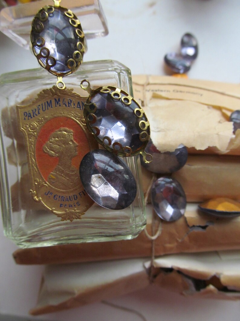 May include: A vintage glass bottle with a gold label that reads "PARFUM MARIAN J.S. GIRAUD FILS PARIS". The bottle is decorated with a chain of oval-shaped, clear glass rhinestones with gold metal settings.