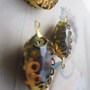 Pode incluir: Tr&ecirc;s enfeites de metal dourado com um centro de vidro castanho escuro. Os enfeites t&ecirc;m um design decorativo e ornamentado.
