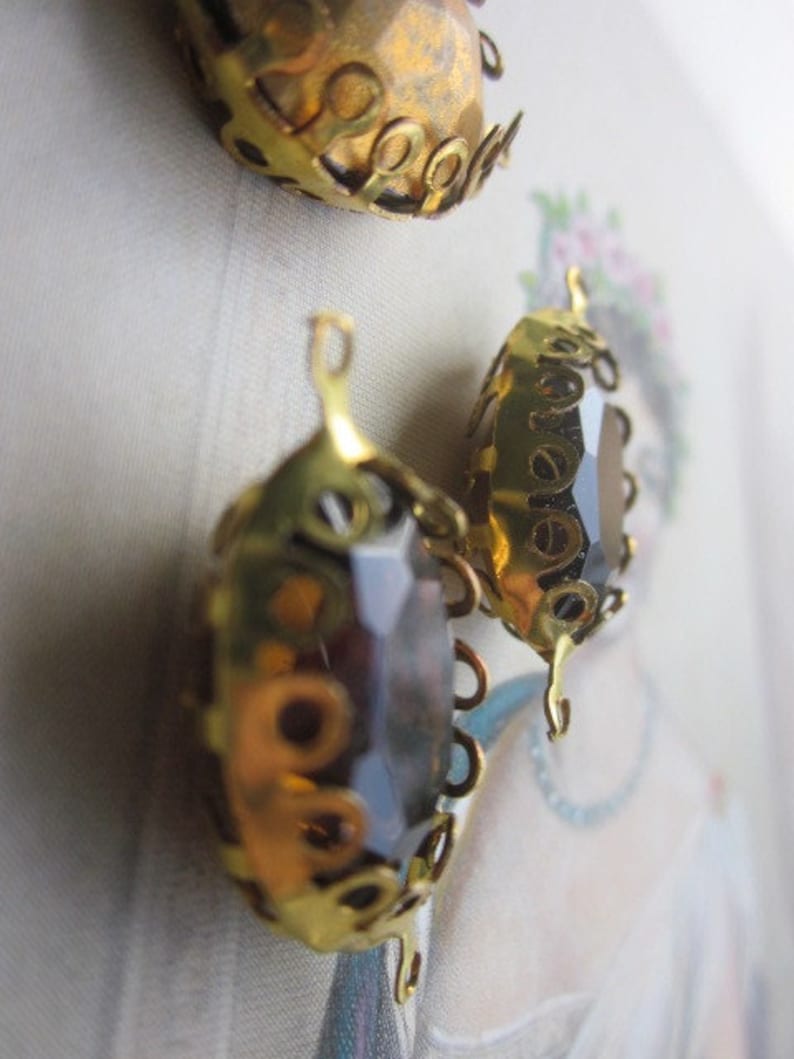 Pode incluir: Tr&ecirc;s enfeites de metal dourado com um centro de vidro castanho escuro. Os enfeites t&ecirc;m um design decorativo e ornamentado.
