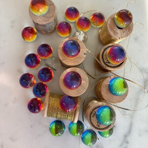 Peut inclure: Une collection de billes en verre iris&eacute;es de diff&eacute;rentes couleurs, dont le rouge, l'orange, le jaune, le vert, le bleu et le violet. Les billes sont dispos&eacute;es sur des bobines de fil d'or.