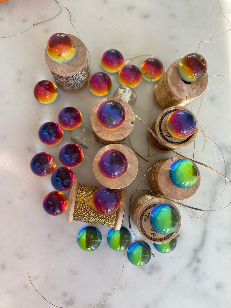 Peut inclure: Une collection de billes en verre iris&eacute;es de diff&eacute;rentes couleurs, dont le rouge, l'orange, le jaune, le vert, le bleu et le violet. Les billes sont dispos&eacute;es sur des bobines de fil d'or.