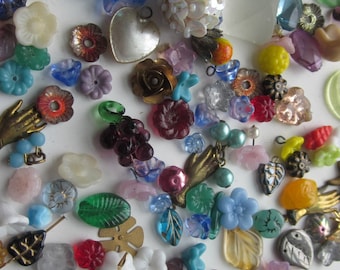 May include: Assortment of colorful glass, metal, and plastic beads and charms. The beads are in various shapes, including hearts, flowers, leaves, and butterflies. Some beads have a metallic finish, while others are clear or opaque.