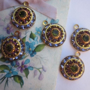 May include: Five gold-toned round pendants with a green and purple rhinestone design. Each pendant has a loop at the top for attaching to a chain or other jewelry.