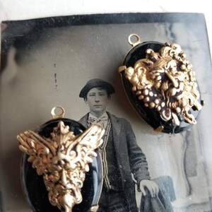 May include: Two black cameo pendants with gold-toned winged griffin designs. The griffins have detailed faces and wings.