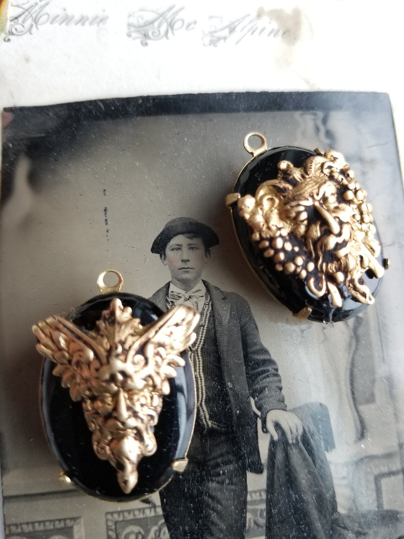 May include: Two black cameo pendants with gold-toned winged griffin designs. The griffins have detailed faces and wings.