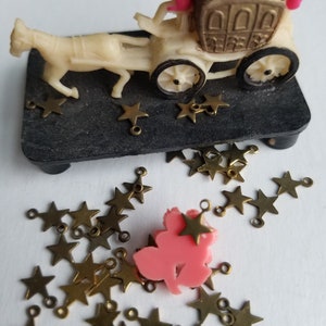 K&ouml;nnte beinhalten: Eine wei&szlig;e Plastikkutsche mit zwei Figuren darin, ein Pferd zieht die Kutsche und goldene sternf&ouml;rmige Charms liegen verstreut herum.
