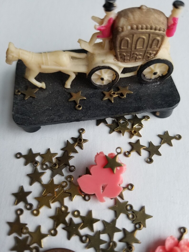 K&ouml;nnte beinhalten: Eine wei&szlig;e Plastikkutsche mit zwei Figuren darin, ein Pferd zieht die Kutsche und goldene sternf&ouml;rmige Charms liegen verstreut herum.
