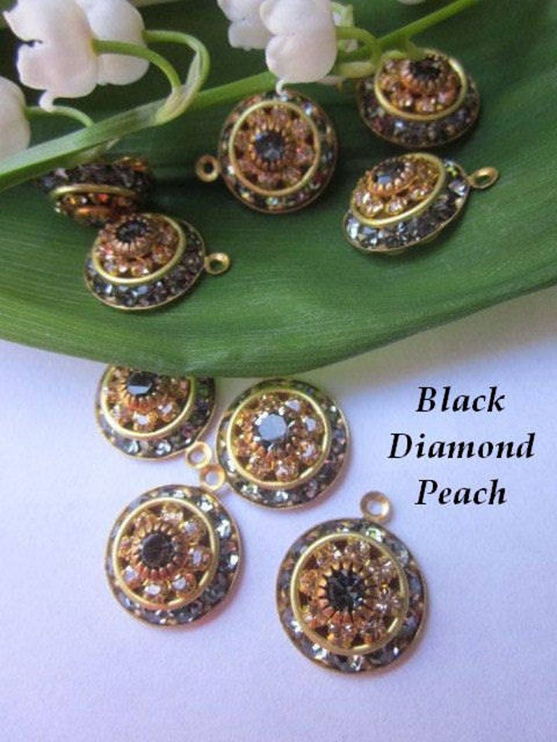 May include: Assortment of round, gold-toned metal charms with black and peach colored rhinestones. The charms have a flower-like design with a central black rhinestone surrounded by smaller peach rhinestones.