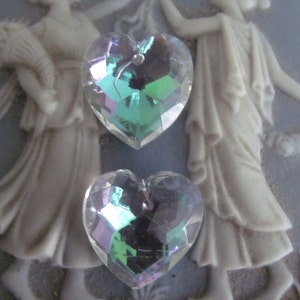 May include: Two iridescent heart-shaped crystal charms with a faceted design. The charms are on a light blue background.