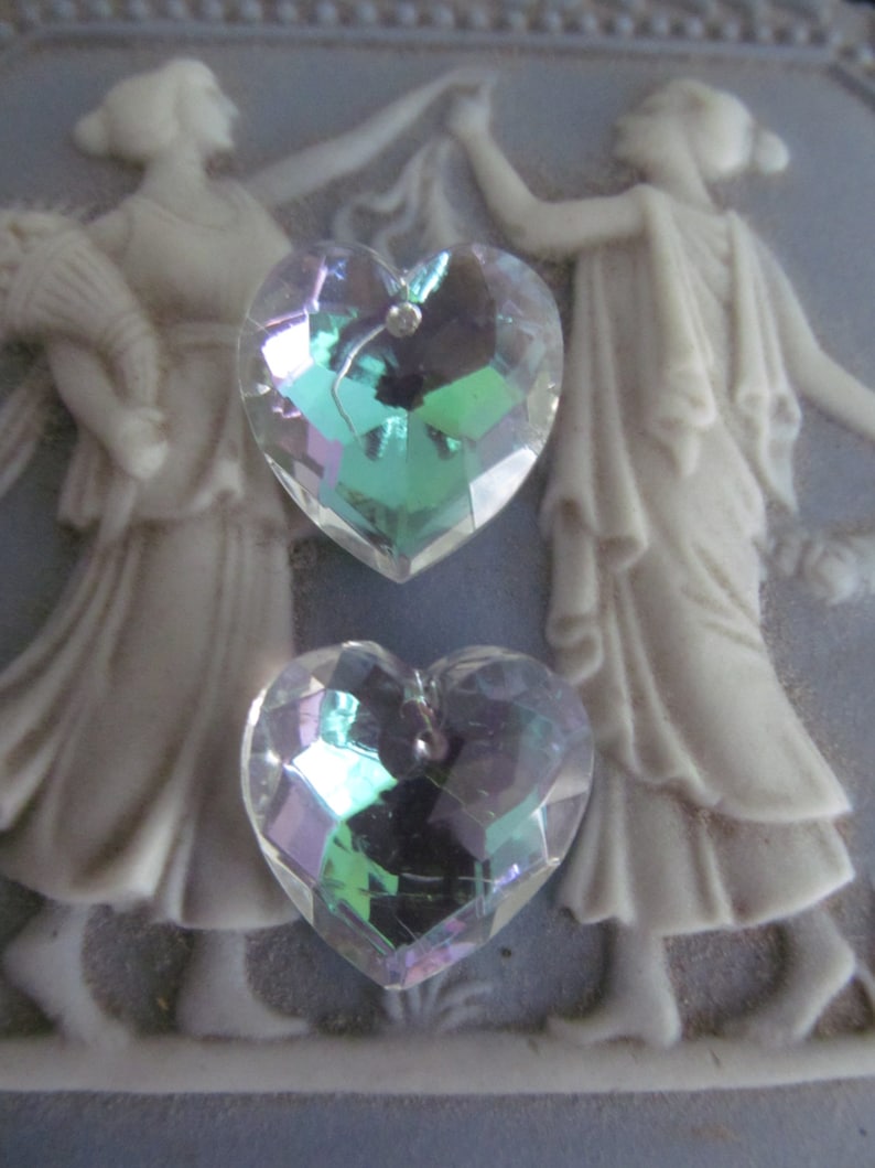 May include: Two iridescent heart-shaped crystal charms with a faceted design. The charms are on a light blue background.