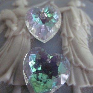 May include: Two iridescent heart-shaped crystal charms. One charm is a light blue and purple color, the other is a dark green and purple color.