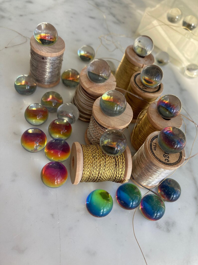 Peut inclure: Une collection de billes en verre color&eacute;es sur des bobines de fil d'or et d'argent. Les billes sont iris&eacute;es et ont un effet arc-en-ciel. Les bobines sont en bois et ont un aspect vintage.