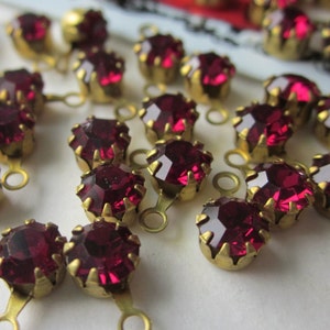 May include: A close-up of a group of red rhinestone embellishments with gold settings. The rhinestones are arranged in a random pattern and have a shiny, faceted surface.