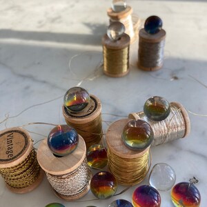 Peut inclure: Assortiment de billes en verre iris&eacute;es sur des bobines de fil d'or et d'argent. Les bobines sont en bois et ont un aspect vintage. Les billes sont de diff&eacute;rentes nuances de bleu, vert et rouge.