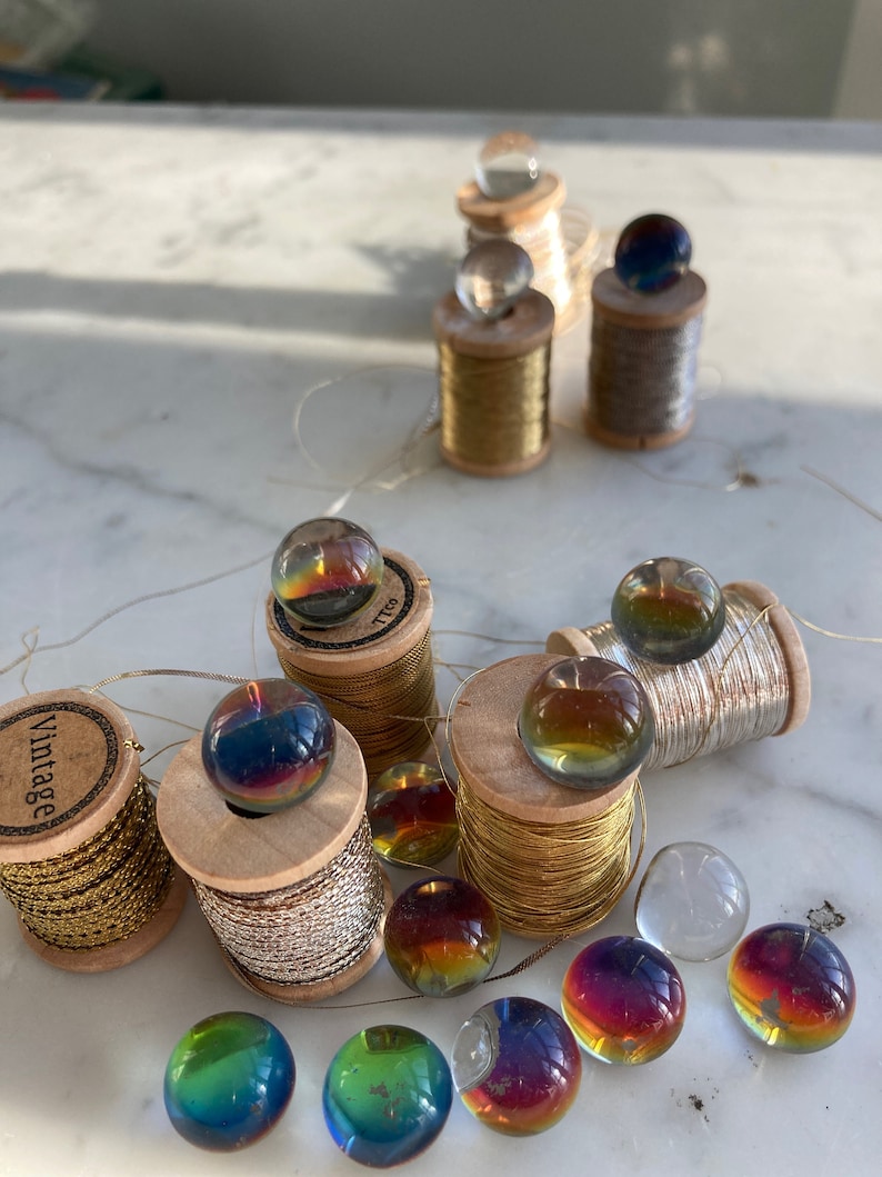 Peut inclure: Assortiment de billes en verre iris&eacute;es sur des bobines de fil d'or et d'argent. Les bobines sont en bois et ont un aspect vintage. Les billes sont de diff&eacute;rentes nuances de bleu, vert et rouge.