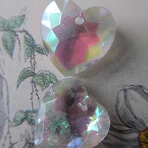 May include: Two iridescent heart-shaped glass charms with a faceted design. The charms are clear with a pink and green iridescent sheen.