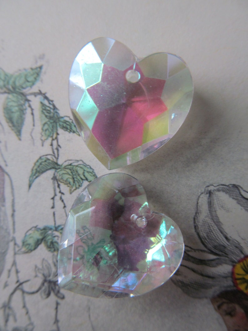 May include: Two iridescent heart-shaped glass charms with a faceted design. The charms are clear with a pink and green iridescent sheen.